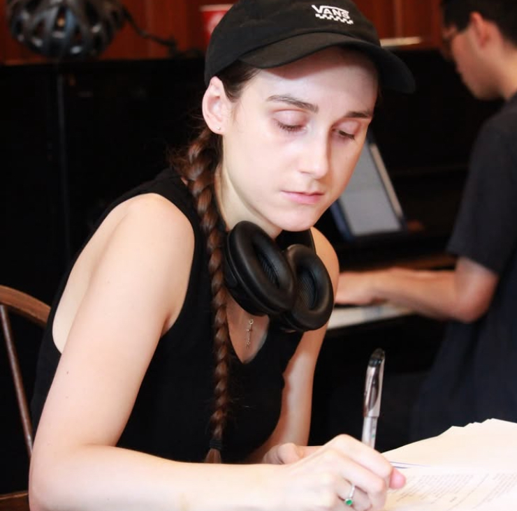 Autumn Rennie taking notes and wearing a cap. In the background is musical director, Jonah Nung at the piano.