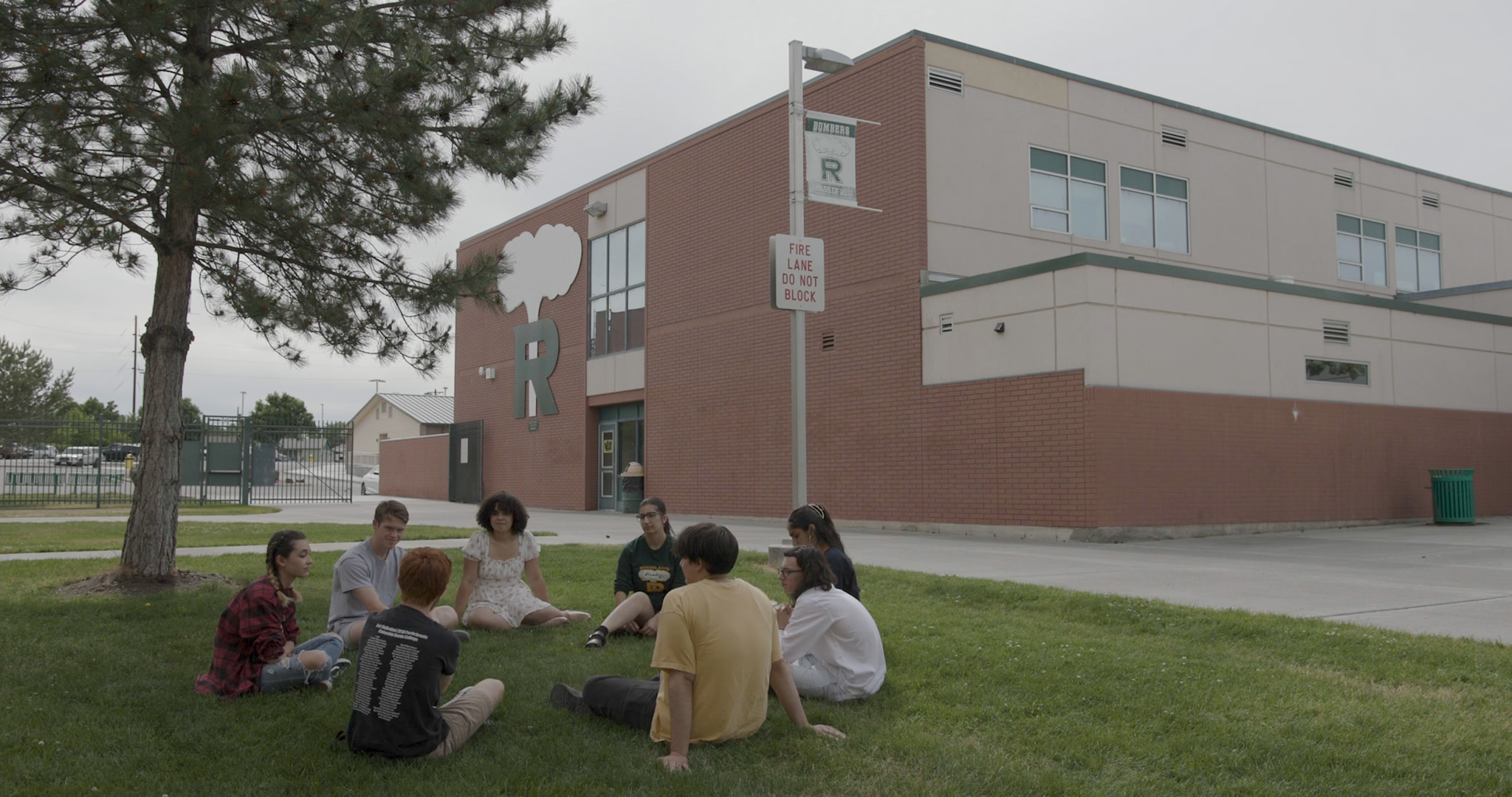 A group of students sitting on the grass in front of a school building in Richland, with an atomic cloud mural on the wall.